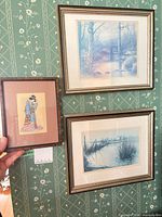 Three framed prints on wall, two blue landscapes and one Japanese lady print