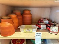 Shelf view showing four terracotta canisters, Le Creuset dish, and three red mini casseroles