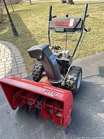 Front view of MTD Yard Machines red two-stage snowblower showing intake, augers, chute, handles and tires