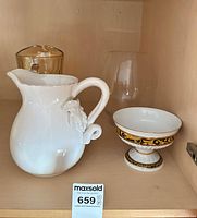 All four items on shelf: white ceramic pitcher, porcelain pedestal bowl, clear glass vase, portion of amber pitcher visible