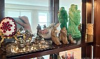 shelf displaying miniature silver tea set, porcelain mudmen figures, swan dish, green figurines, beaded plaque