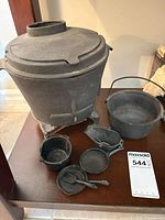 Overall lot showing pot-belly stove, cauldron, skillet, pots and cup