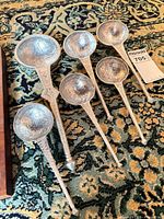 Six embossed metal ladles arranged on patterned carpet