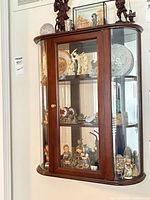 Front view of wooden curio cabinet hung on wall, showing glass door, shelves, contents not included