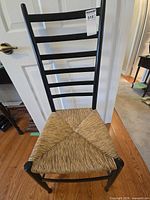 Full front view of black ladder-back chair with woven seat