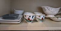 Shelf with square plates, grey bowl, stack of small dishes, three oriental cups, white embossed gravy boat