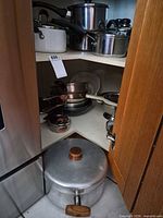 Corner cabinet showing multiple cookware pieces: saucepans, fry pans, colanders, aluminum Dutch oven