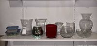Shelf with assorted glass vases, red vase, metallic votive, plastic containers with gems