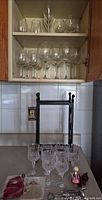 Cabinet shelves with assorted stemware; counter with crystal goblets, metal wine rack, small bar accessories