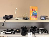 Full view of both shelves showing binoculars, travel iron, reading light, luggage scales, clocks and book