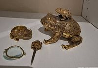 All items grouped: large frog box, smaller frog box opened in two parts, stick pin, magnifier