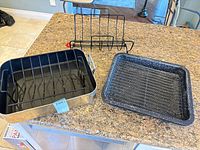 Large metal roasting pan with V-rack beside smaller enamel pan and rib rack