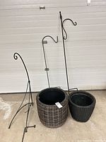 two resin wicker planters and three black metal shepherd hooks