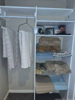 Closet view showing two crochet tablecloths hanging and stacks of placemats and linens on shelving
