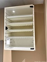 Front view of wall-mounted white storage cabinet with transparent door and four pull-out trays