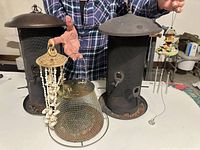 Front view of two large black feeders, smaller brass-tone feeder, seashell chime and mini chime