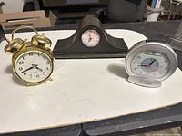 Overview of three clocks: gold twin-bell, dark wood mantel, silver alarm
