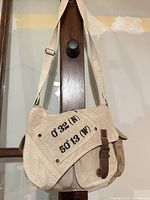 Front view of beige canvas messenger bag showing printed coordinates, flap and adjustable strap