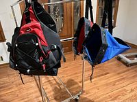 Two sling backpacks hanging on rack, red-black and blue-black colorways visible