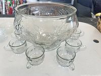 Clear pressed glass punch bowl surrounded by handled cups