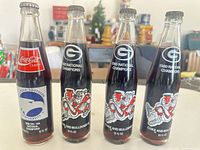 Front view of all four sealed commemorative bottles showing team logos and champion text