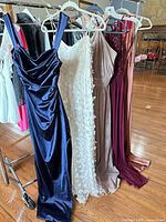 Five floor-length gowns on rack showing full lot