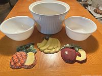 Front view of three white bowls and three fruit plaques arranged on table