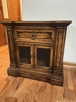 Front view of nightstand showing drawer, mesh doors, paneled sides, plinth base