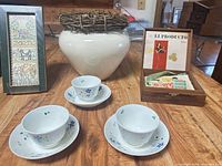 Group shot of vase, framed print, porcelain cups/saucers, and open cigar box with stamps visible