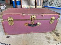 front view of red steamer trunk with brass-tone hardware and black handle