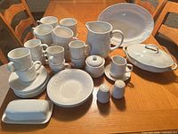 Full set arranged on table displaying plates, mugs, pitcher, covered dish, platter, butter dish, sugar, creamer, and shakers
