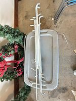 Stack of four white metal sectional curtain rods on a gray tote