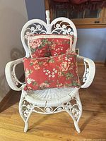 Front view of white wicker chair with two red floral cushions