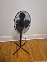 Full view of black pedestal fan showing cross base, pole and head
