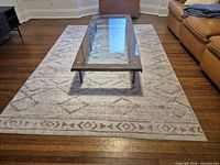 Full view of rectangular beige/ivory geometric rug under glass coffee table