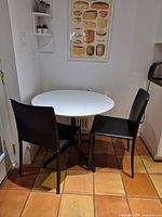 Full view of round white table with two black chairs