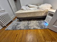 Full view of gray shag rug placed under bed showing overall size and color