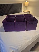 Six purple fabric storage cubes side-by-side on bed