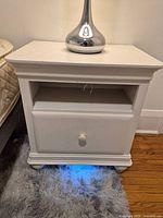 Front view of Smartstuff white nightstand showing drawer, open shelf, illuminated base