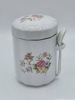 Front view of floral ceramic canister with lid and spoon attached