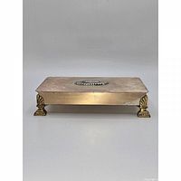 Front view of closed rectangular silver-plated box on four feet showing sunburst medallion and surface wear