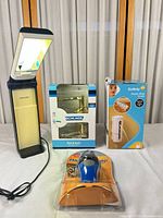 All four items grouped: Ott-Lite lamp open, Schlage lever set boxed, Safety 1st cover boxed, Staples stapler packaged