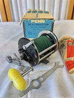 Reel spooled with green line, yellow handle knob, wrench tool and paper insert visible