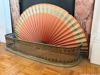 Brass fender and paper fan in front of fireplace