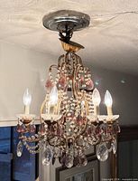 Full view of chandelier installed, showing brass frame, pink and clear crystals, four bulbs