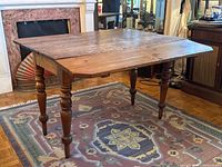 Oblique view of fully extended pine drop-leaf table showing turned legs and plank top