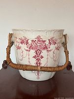 Front view of ironstone slop pail showing floral red transferware pattern and cane handle