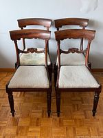Front view of all four walnut dining chairs showing mixed upholstery and carved backs