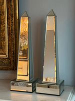 Both mirrored obelisks side by side showing dimensions and reflective surfaces