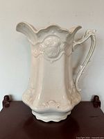 Front view of white ironstone pitcher showing floral relief and pedestal base